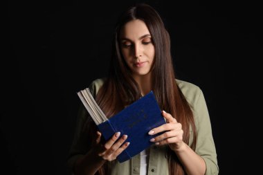 İncil 'i olan güzel bir kadın siyah arka planda dua ediyor.