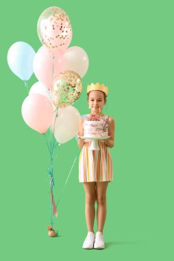 Doğumgünü pastası ve yeşil arka planda balonları olan taç giymiş şirin küçük bir kız.