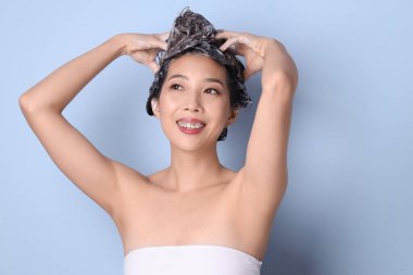 Genç Asyalı kadın mavi arka plana şampuan sürüyor, yakın plan.