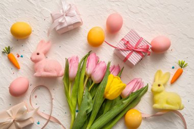 Paskalya yumurtaları hediye kutuları, lale çiçekleri ve beyaz arka planda tavşanlar.