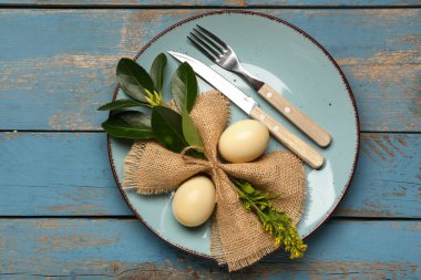 Paskalya yumurtaları, peçete ve çatal bıçak takımları mavi ahşap arka planda.
