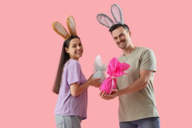 Pembe arka planda Paskalya hediyesi yumurtaları olan tavşan kulaklı mutlu çift.