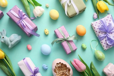 Paskalya yumurtaları, lale çiçekleri hediye kutuları ve turkuaz arka planda tavşan.