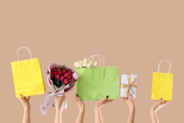 Lale buketleri, alışveriş torbaları ve bej arka planda hediye kutusu olan kadın elleri. Uluslararası Kadınlar Günü