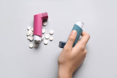 Astım spreyli çocuk eli ve beyaz arka planda haplar.