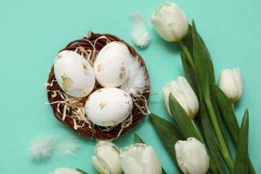 Paskalya yumurtalı yuva, turkuaz arka planda tüyler ve laleler