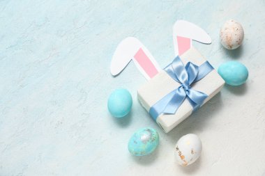Hediye kutusuyla boyanmış Paskalya yumurtaları ve mavi grunge arka planında kağıt tavşan kulakları.
