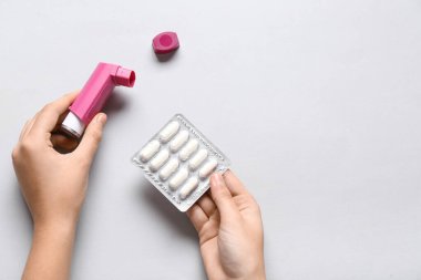 Astım spreyli çocuk elleri ve beyaz arka planda haplar.