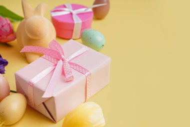 Paskalya hediyeleri, boyalı yumurtalar ve sarı arka planda tavşan figürü.