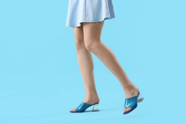 Renkli arka planda mavi sandaletli genç bir kadının bacakları