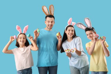 Mavi arka planda Paskalya yumurtaları olan tavşan kulaklı mutlu bir aile.