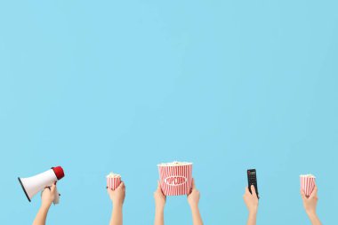 Patlamış mısır, uzaktan kumanda ve mavi arka planda megafon bulunan kovaları tutan eller.