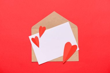 Zarfta boş kart ve kırmızı zemin üzerinde kağıt kalpler var. Sevgililer Günü kutlaması