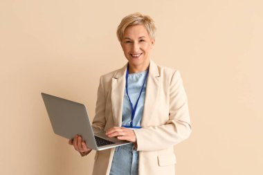 Olgun kadın programcı bej arka planda dizüstü bilgisayarla çalışıyor