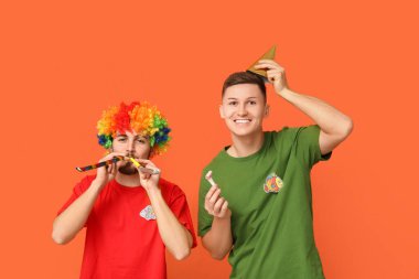 Kağıt balıklarla kılık değiştirmiş genç arkadaşlar ve turuncu arka planda parti ıslıkları. 1 Nisan kutlamaları