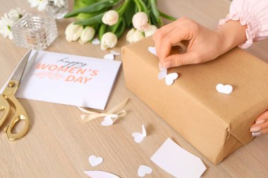Uluslararası Kadınlar Günü için hediye paketi hazırlayan kadın ahşap masada, yakın plan.