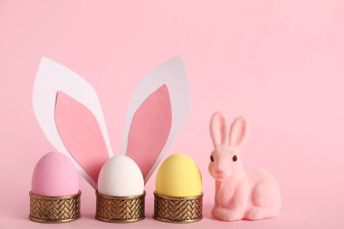 Paskalya yumurtası, tavşan ve pembe arka planda kağıt kulaklı tutucular.