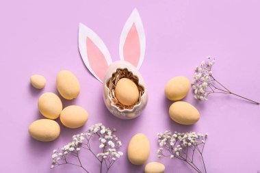 Boyanmış Paskalya yumurtaları, çingene çiçekleri ve mor arka planda kağıt tavşan kulakları.