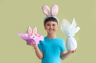 Paskalya pastası ve yeşil arka planda hediye yumurtası takan sevimli küçük bir çocuk.