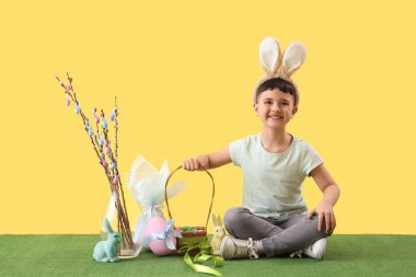 Cute little boy wearing bunny ears with Easter basket, gift egg and pussy willow branches on yellow background
