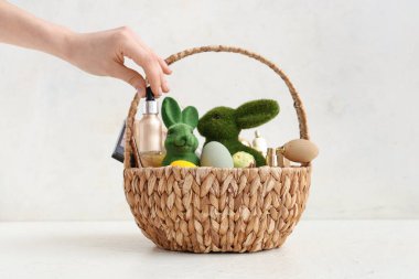 Dekoratif kozmetiklerle dolu sepeti olan kadın eli, beyaz arka planda paskalya yumurtaları ve tavşancıklar.