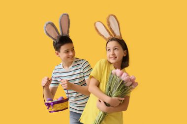 Tavşan kulaklı küçük çocuklar Paskalya yumurtaları ve sarı arka planda laleler