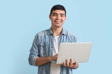 Mavi arka planda dizüstü bilgisayar kullanan mutlu genç adam.