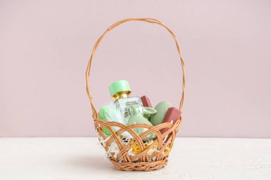 Dekoratif kozmetik ürünleri, Paskalya yumurtaları ve pembe duvarın yanındaki beyaz masada duran tavşan sepeti.