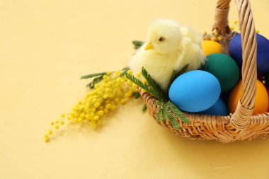 Boyanmış Paskalya yumurtaları, mimoza ve sarı arka planda civciv dolu sepet.