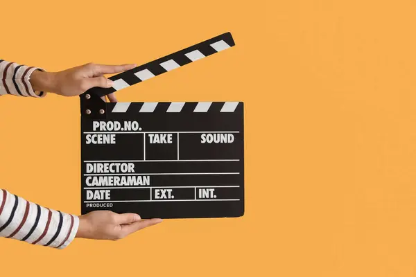 Female hands with movie clapper on yellow background