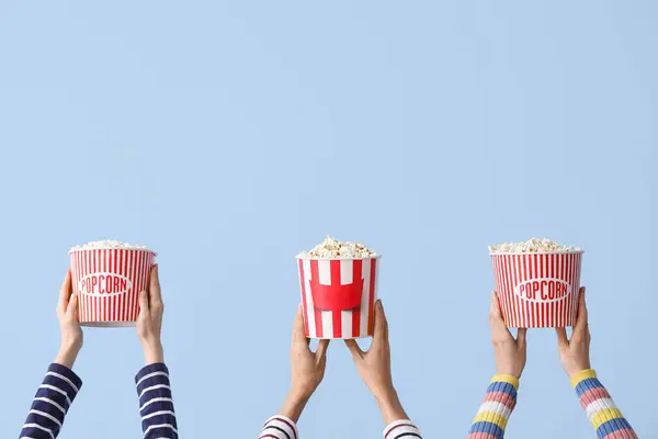 Many hands with buckets of popcorn on blue background