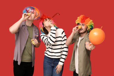 Kırmızı arka planda parti düdüğü ve balonla komik kılık değiştirmiş genç arkadaşlar. 1 Nisan kutlamaları