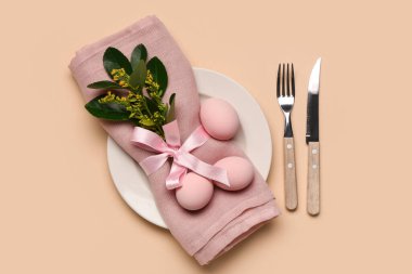 Paskalya yumurtaları, yapraklar ve bej arka planda çatal bıçak seti olan şık bir masa.