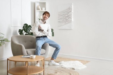 Evdeki yumuşak koltukta oturan laptoplu yakışıklı adam.