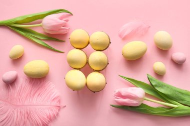 Boyanmış Paskalya yumurtaları, lale çiçekleri ve pembe arka planda tüyleri olan tutucu.