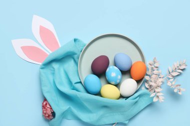 Boyanmış Paskalya yumurtaları, kağıttan tavşan kulakları ve mavi arka planda şakayık çiçekleri olan kompozisyon