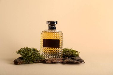 Bej arka planda yosun olan bir şişe parfüm.