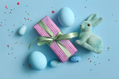 Mavi arka planda tavşan ve hediye kutusu olan Paskalya yumurtaları.