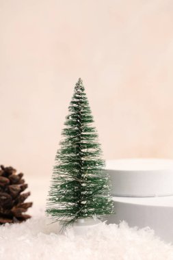 Karlı dekoratif Noel ağacı, alçı podyumlar ve bej grunge arka planda çam kozalağı