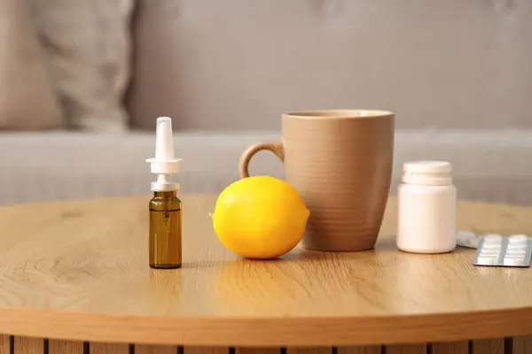 Nasal drops with lemon, cup and pills on table in room, closeup