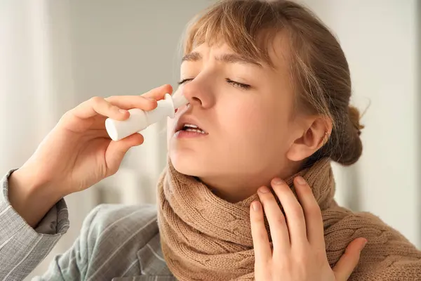 Ill young businesswoman with scarf using nasal drops in office, closeup