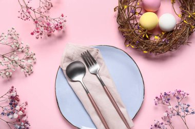 Paskalya için güzel bir masa, pembe arka planda yumurtalar, çiçekler ve çelenkler.