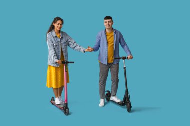 Mavi arka planda modern elektrikli scooterlara binen mutlu genç çift