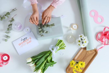Hediye kutusu olan kadın elleri, paketleme malzemeleri ve arka planda güzel çiçekler. Uluslararası Kadınlar Günü