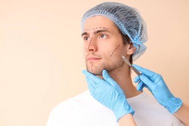 Plastik cerrah, genç adamın yüzünü bej arka planda işaretliyor, yakın plan.