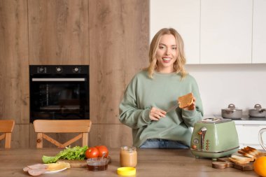 Genç ve güzel bir kadın mutfakta fıstık ezmeli tost yapıyor.