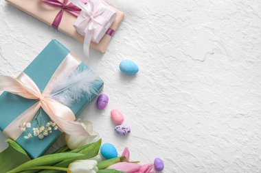 Paskalya yumurtaları hediye kutuları ve beyaz arka planda çiçekler.
