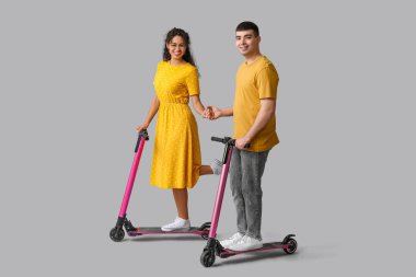 Gri arka planda modern elektrikli scooter kullanan genç ve güzel bir çift.