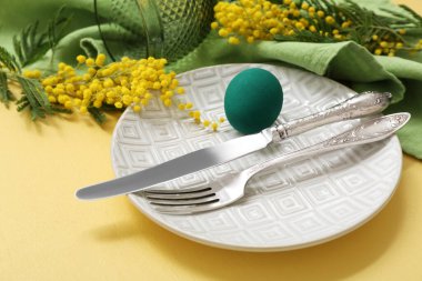 Renkli yumurta, yeşil peçete ve sarı arka planda mimoza ile güzel bir Paskalya sofrası.