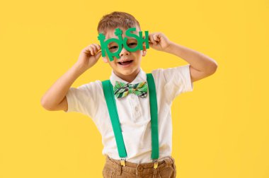 Sarı arka planda yeni gözlüklü şirin bir çocuk. Aziz Patrick Günü kutlaması